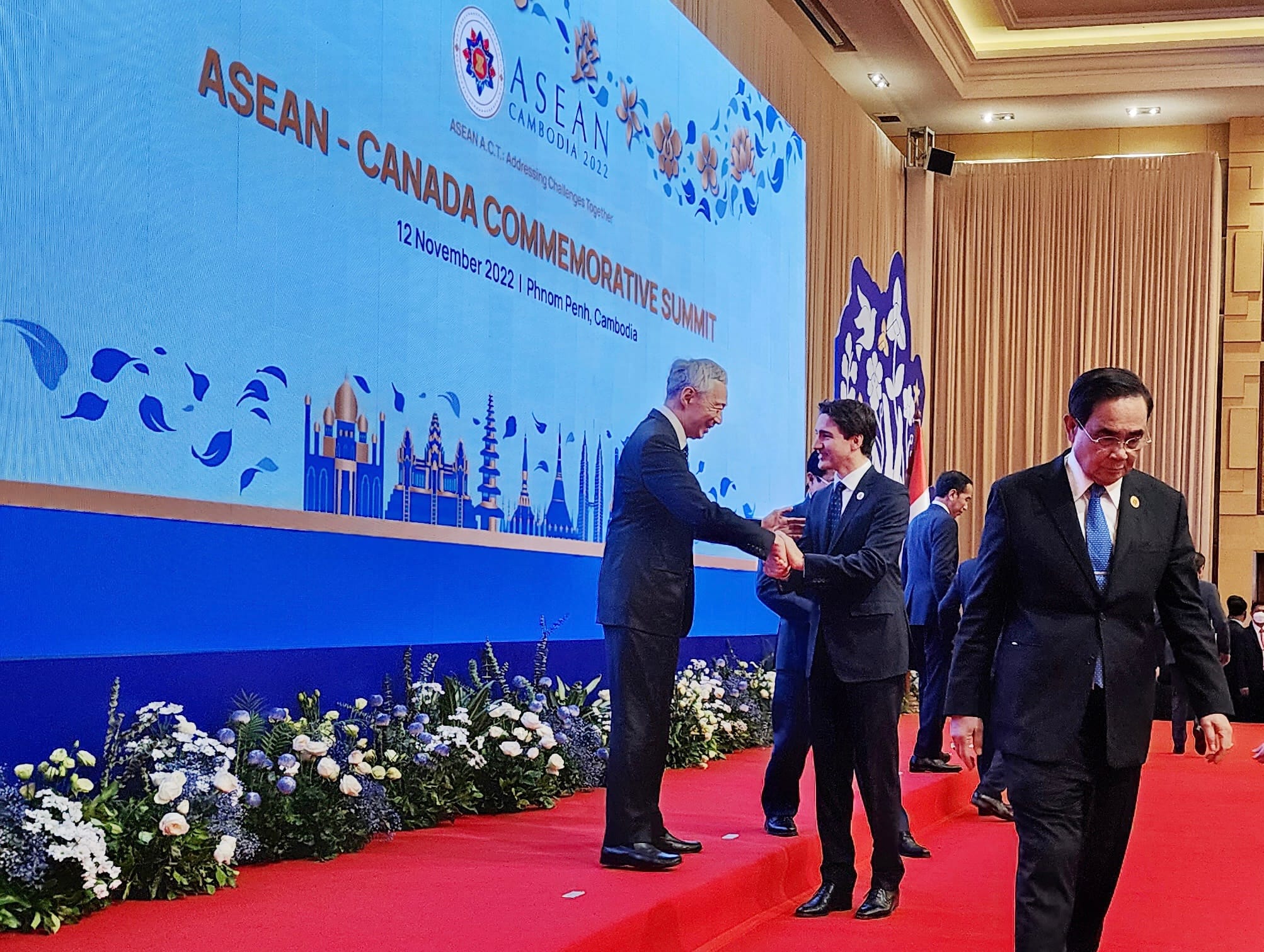 Men in suits shaking hands on a red carpet in front of an ASEAN-Canada summit banner.