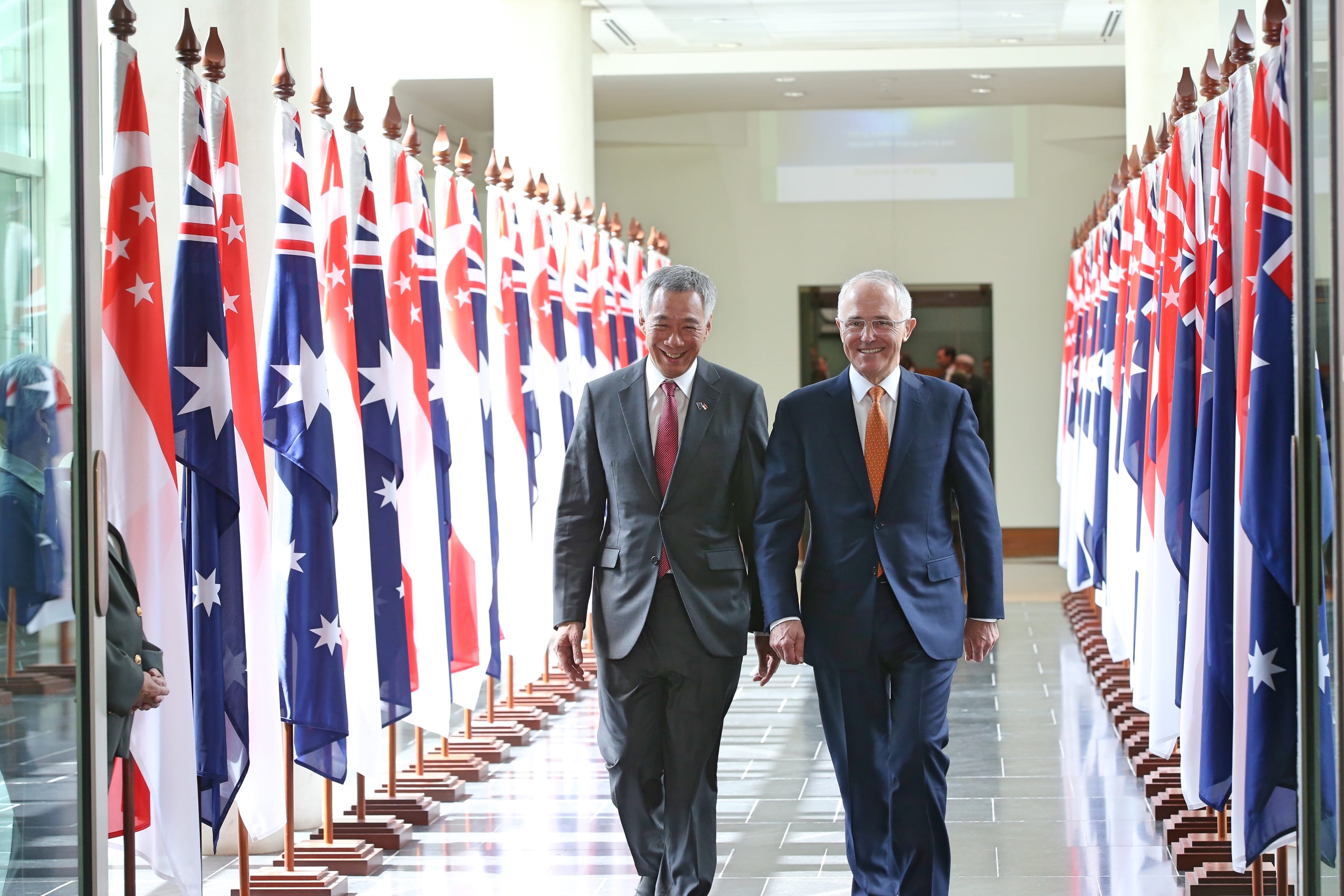 Lee Hsien Loong and Malcolm Turnbull walk flanked by Singaporean and Australian flags.
