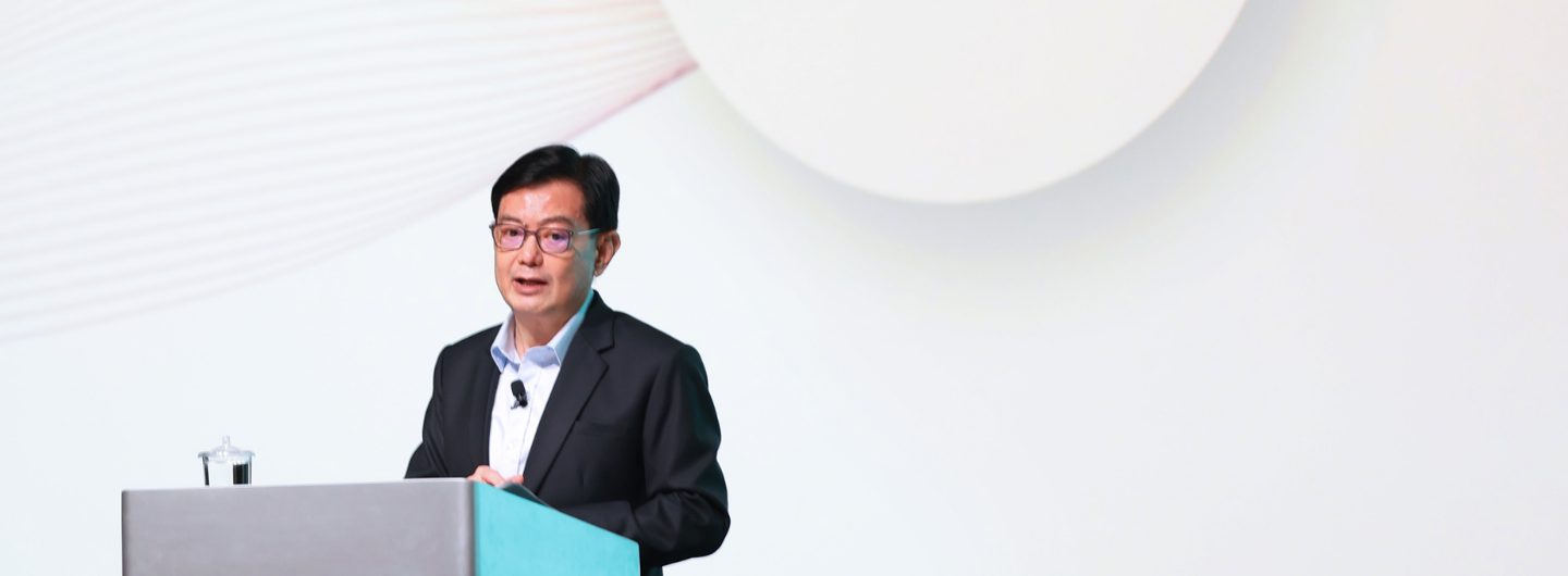 Man in suit at podium with mic against white background.