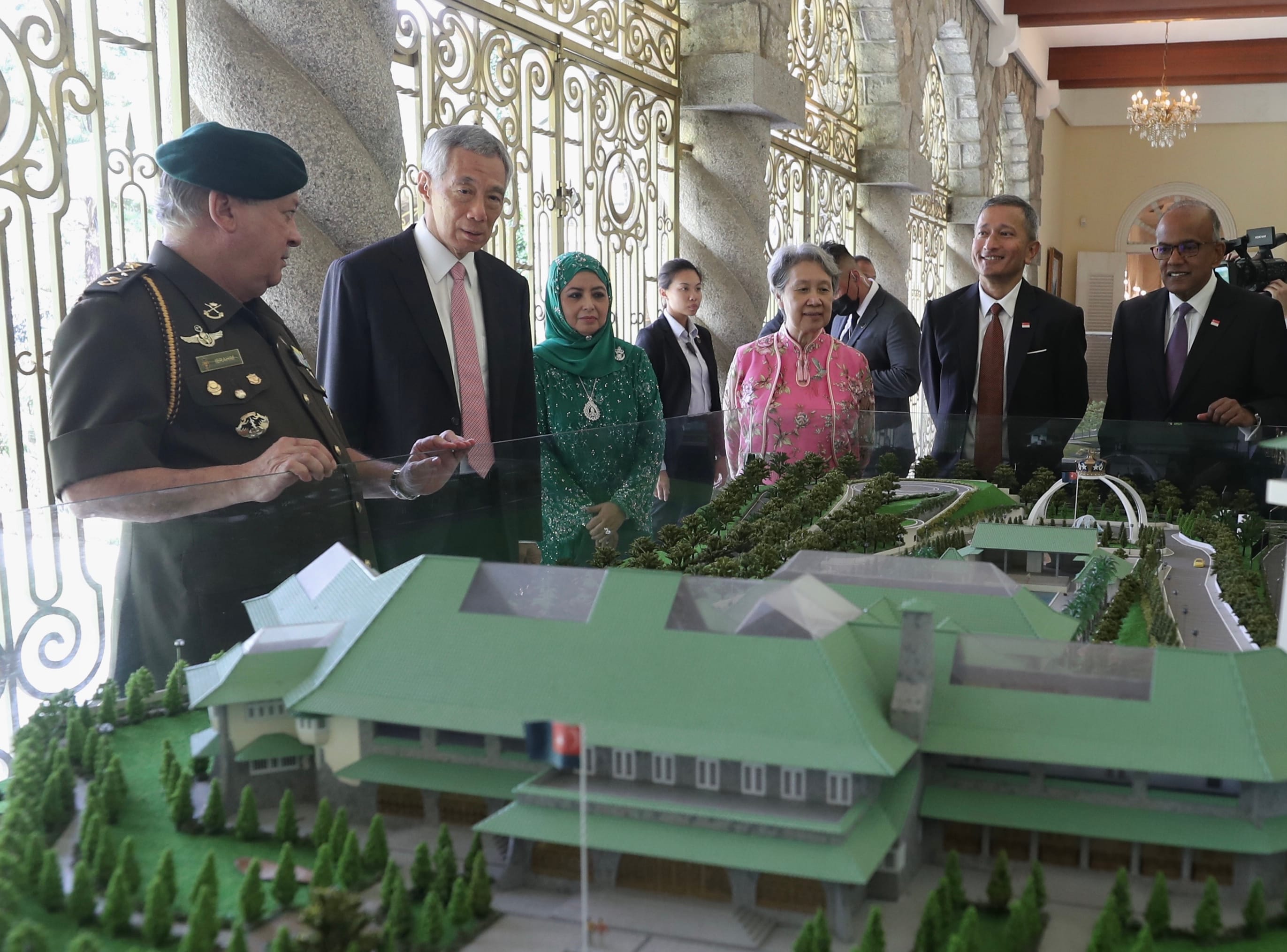 Dignitaries view scaled model of building with green roofs and Malaysian flag on grounds.