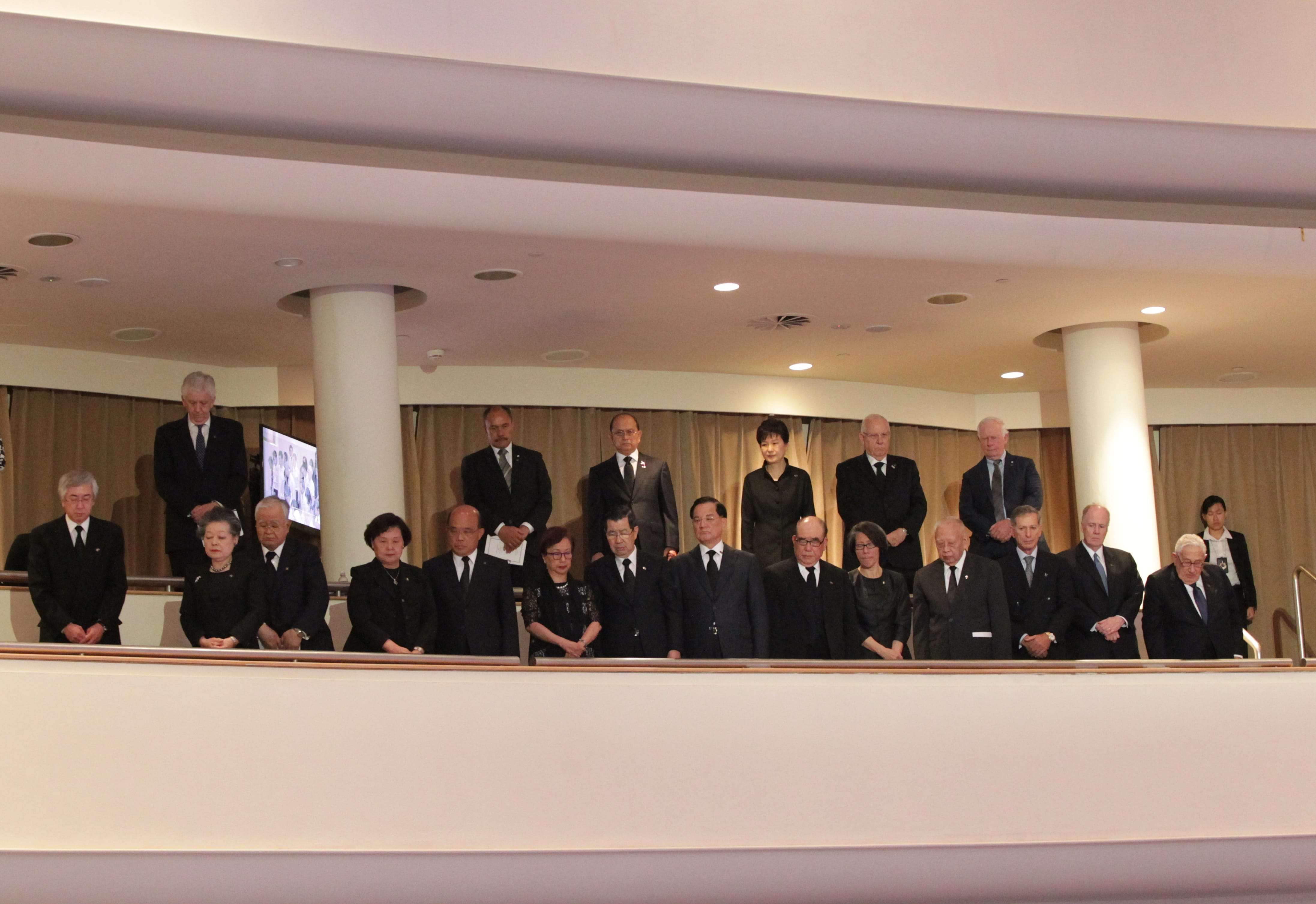 Group of people in dark suits and dresses stand formally on an upper balcony.