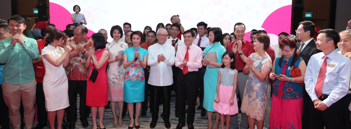 Group of people in formal attire applauding, some wearing traditional Chinese clothing.
