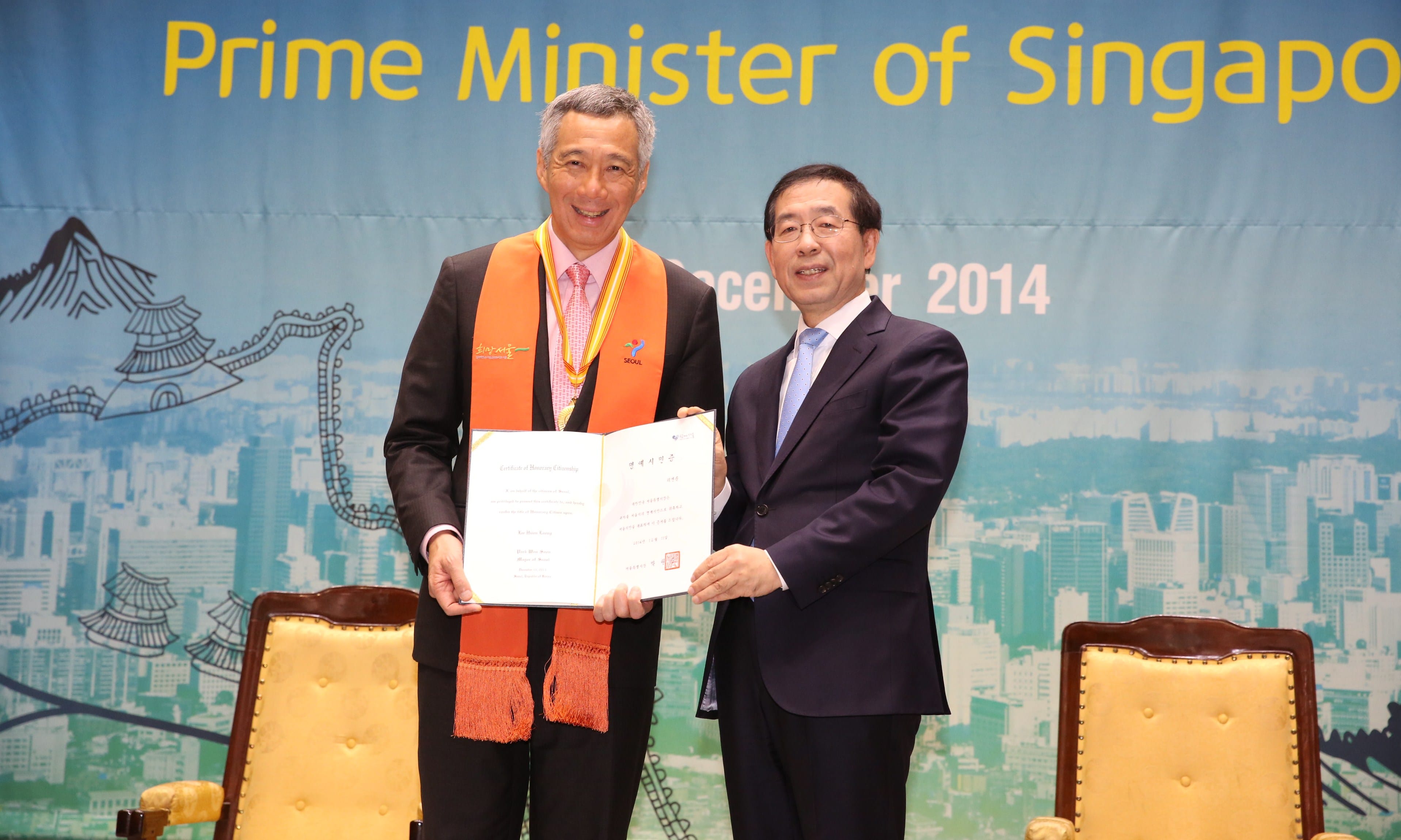 Two men holding certificates, with "Prime Minister of Singapore" banner behind them.