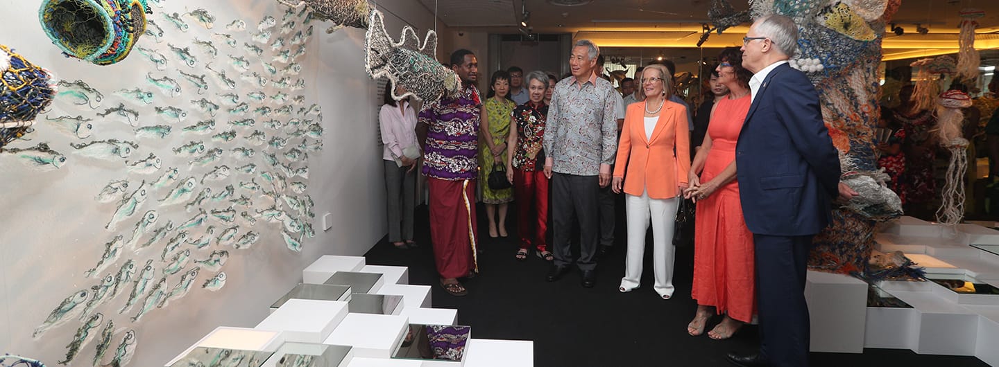 People viewing a wall art installation of crafted fish; white cube pedestal display in foreground.