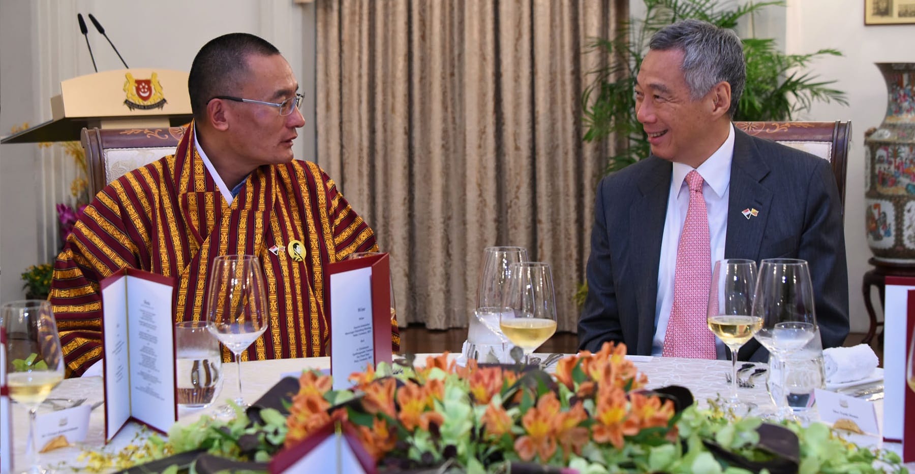 King of Bhutan and Lee Hsien Loong at a formal dinner, floral centerpiece.