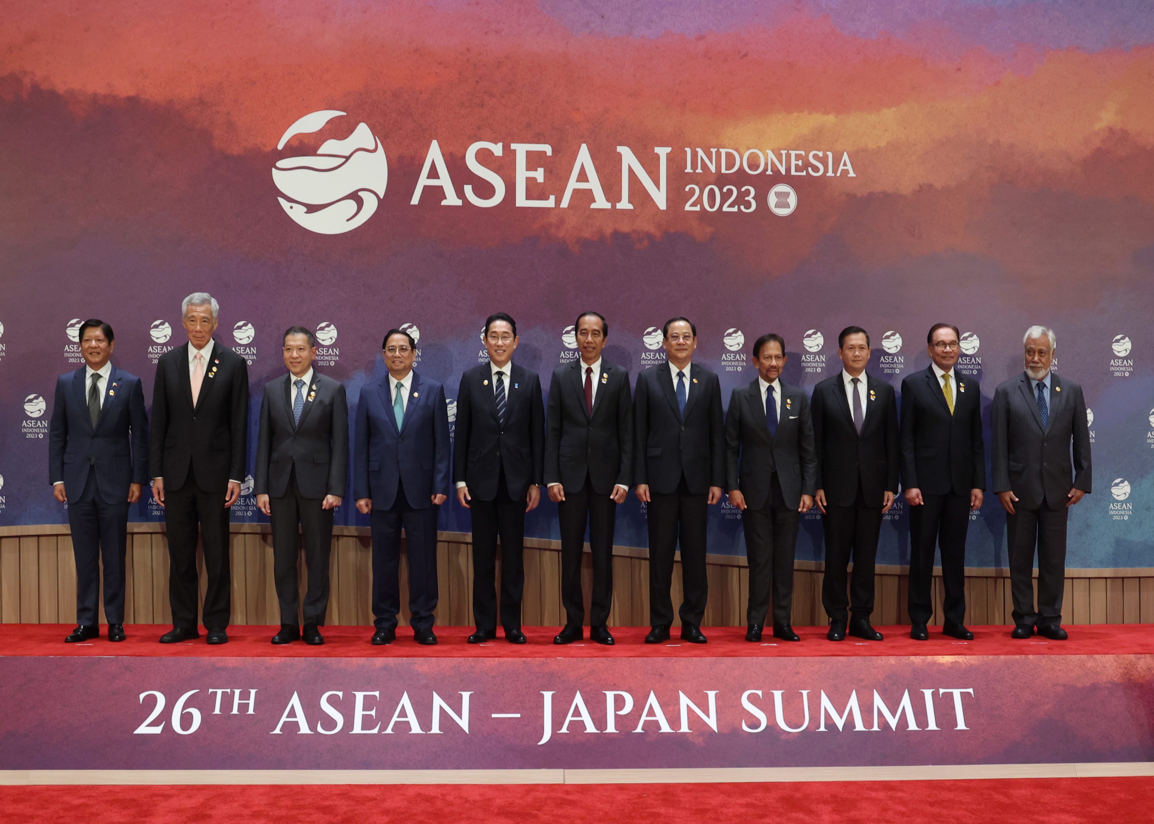 Eleven people in suits stand on a red carpet in front of an "ASEAN Indonesia 2023" banner.