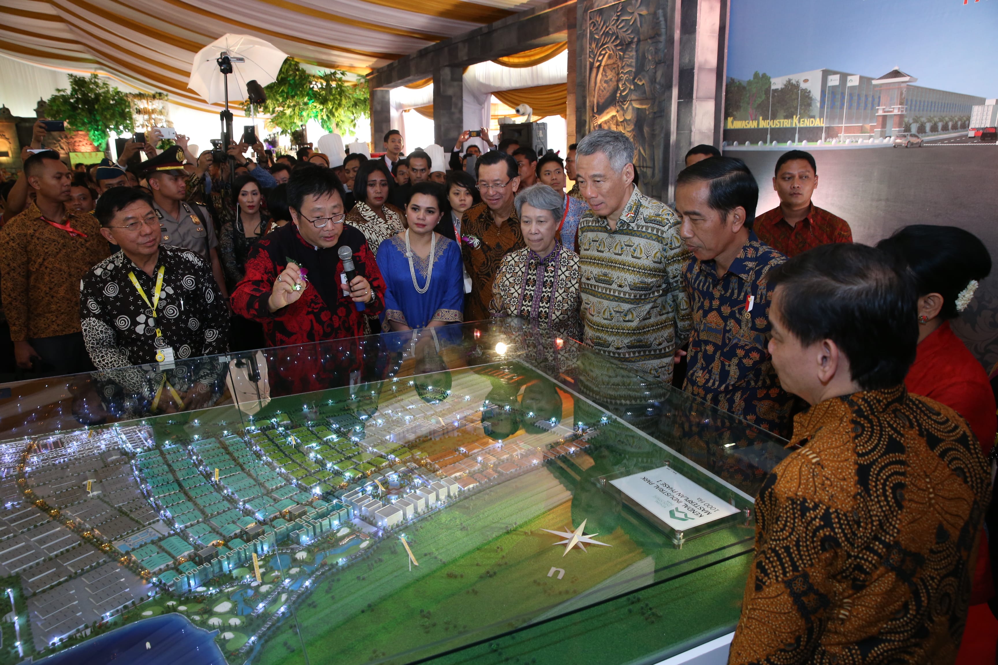 Group viewing "Kawasan Industri Kendal" miniature city; men in batik shirts, speaker with microphone.