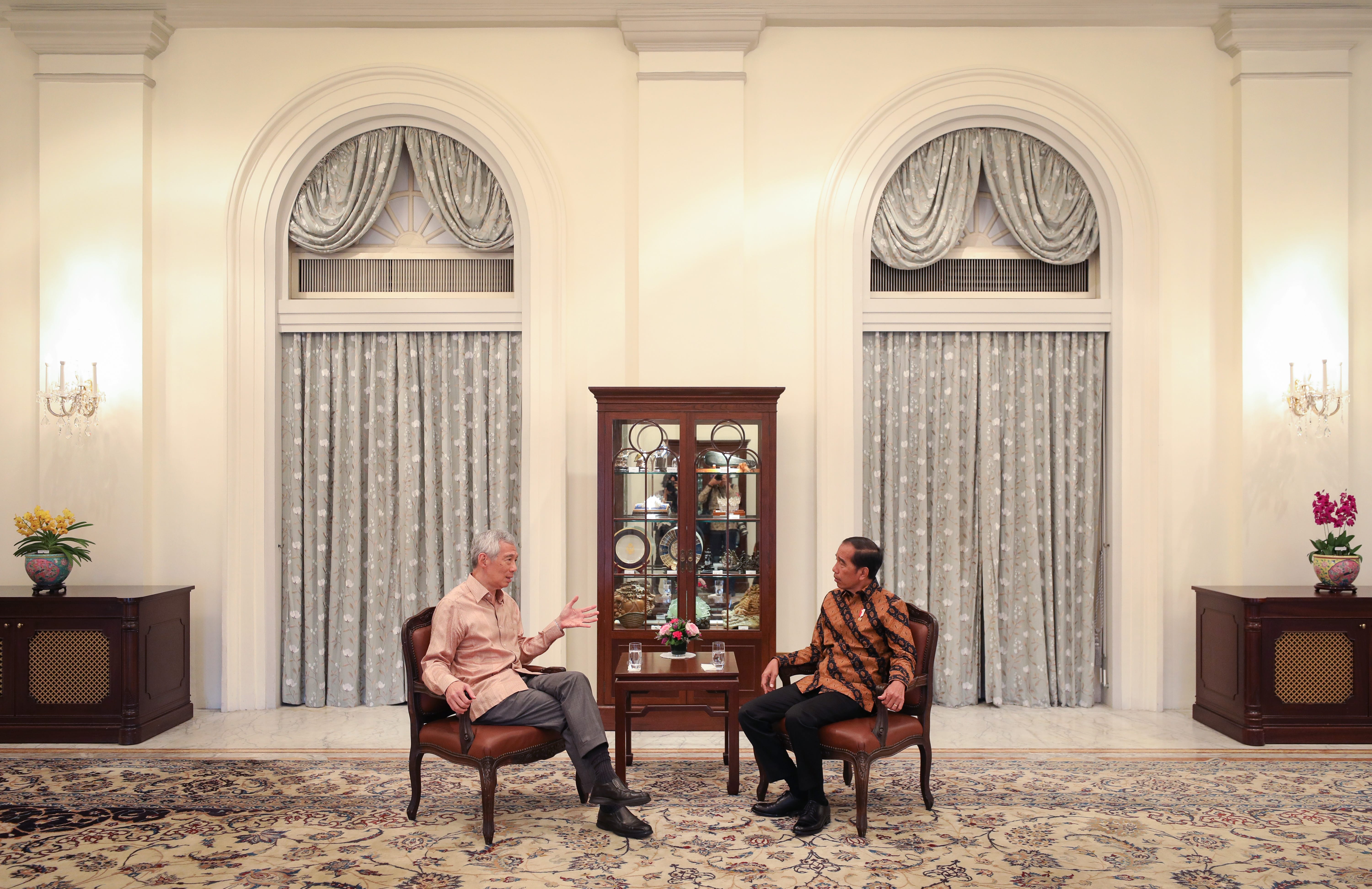 Lee Hsien Loong and Joko Widodo seated in chairs against a windowed backdrop.