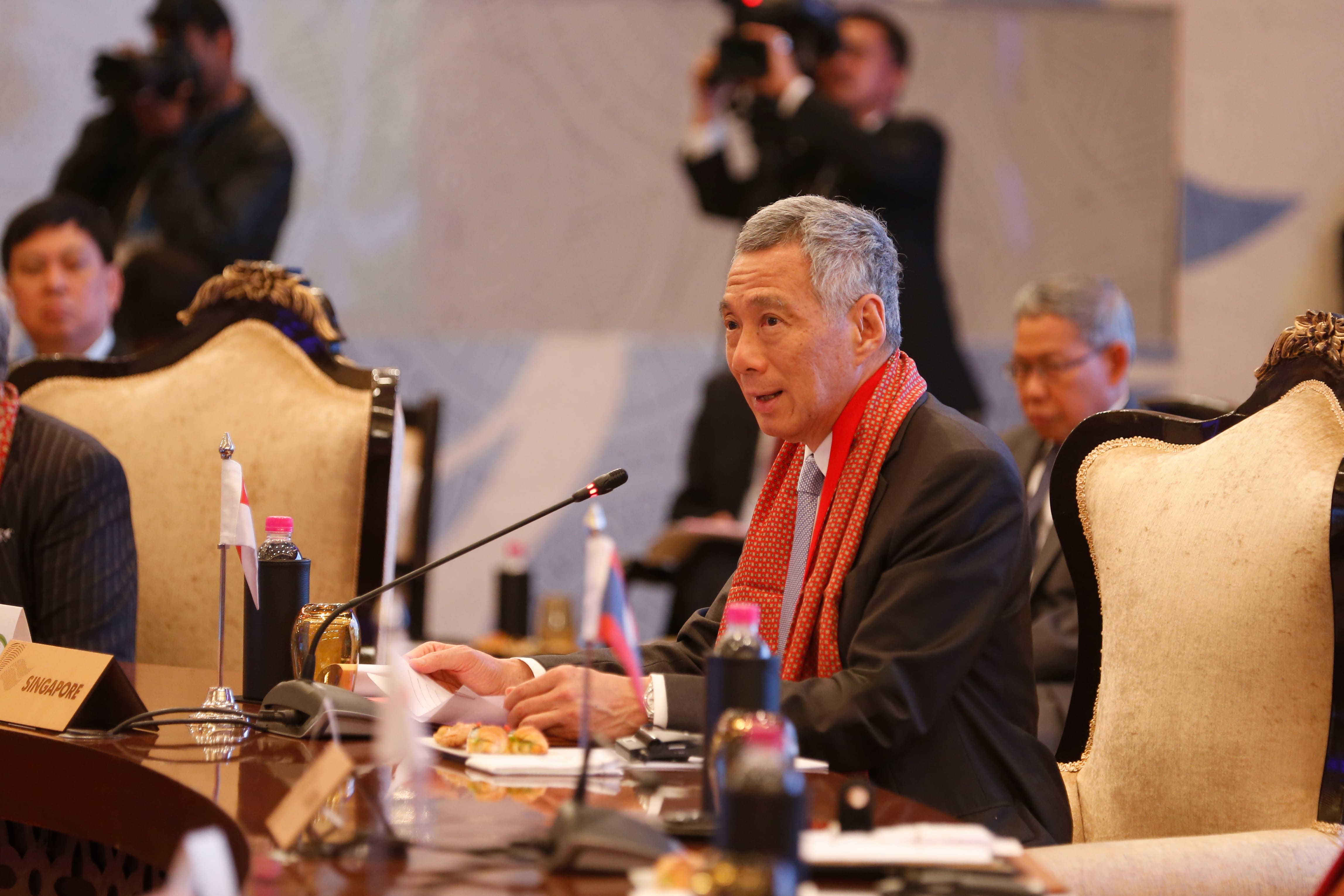 Lee Hsien Loong at a conference table with flags and photographers present.