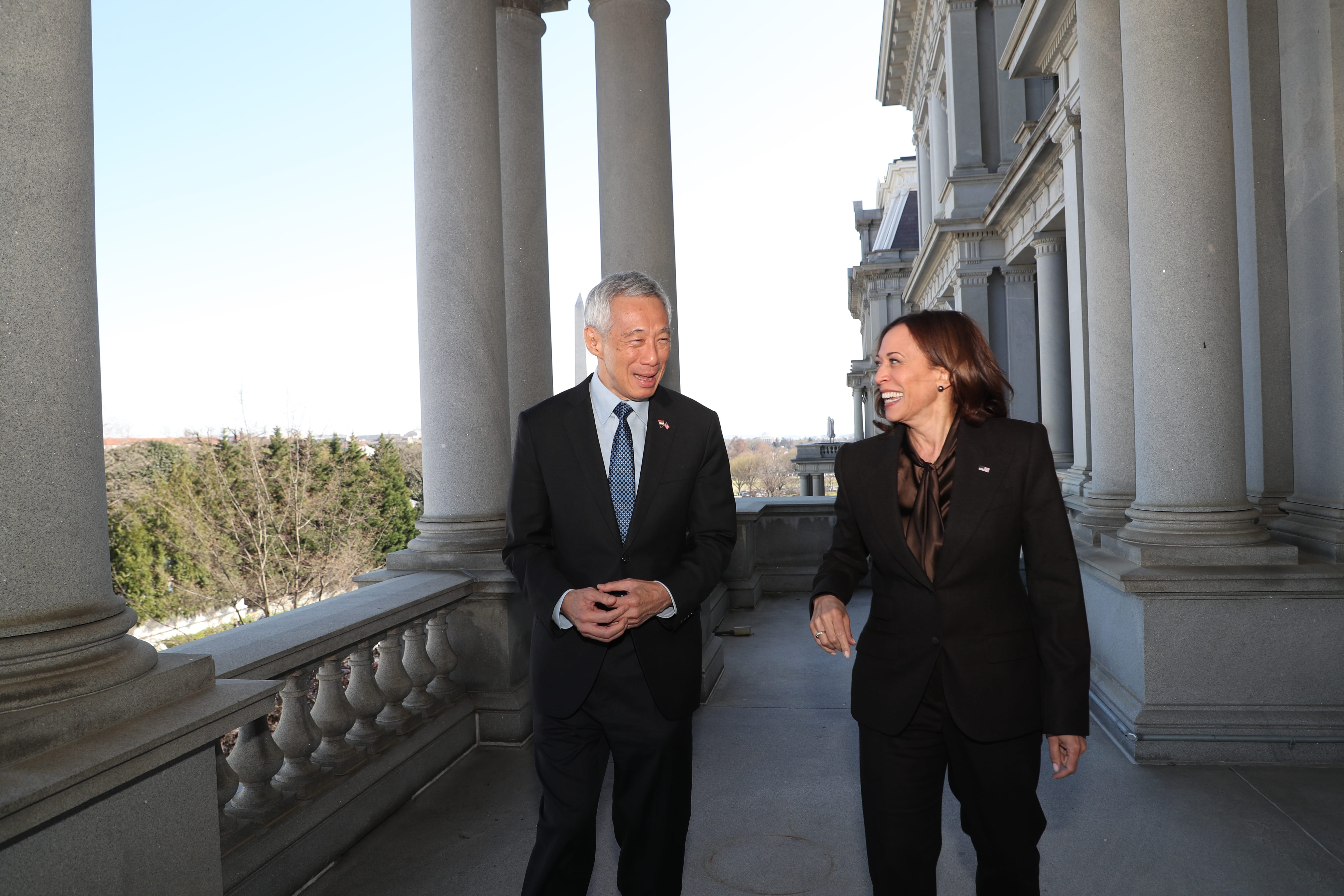 Lee Hsien Loong and Kamala Harris in suits walking on a colonnaded balcony.