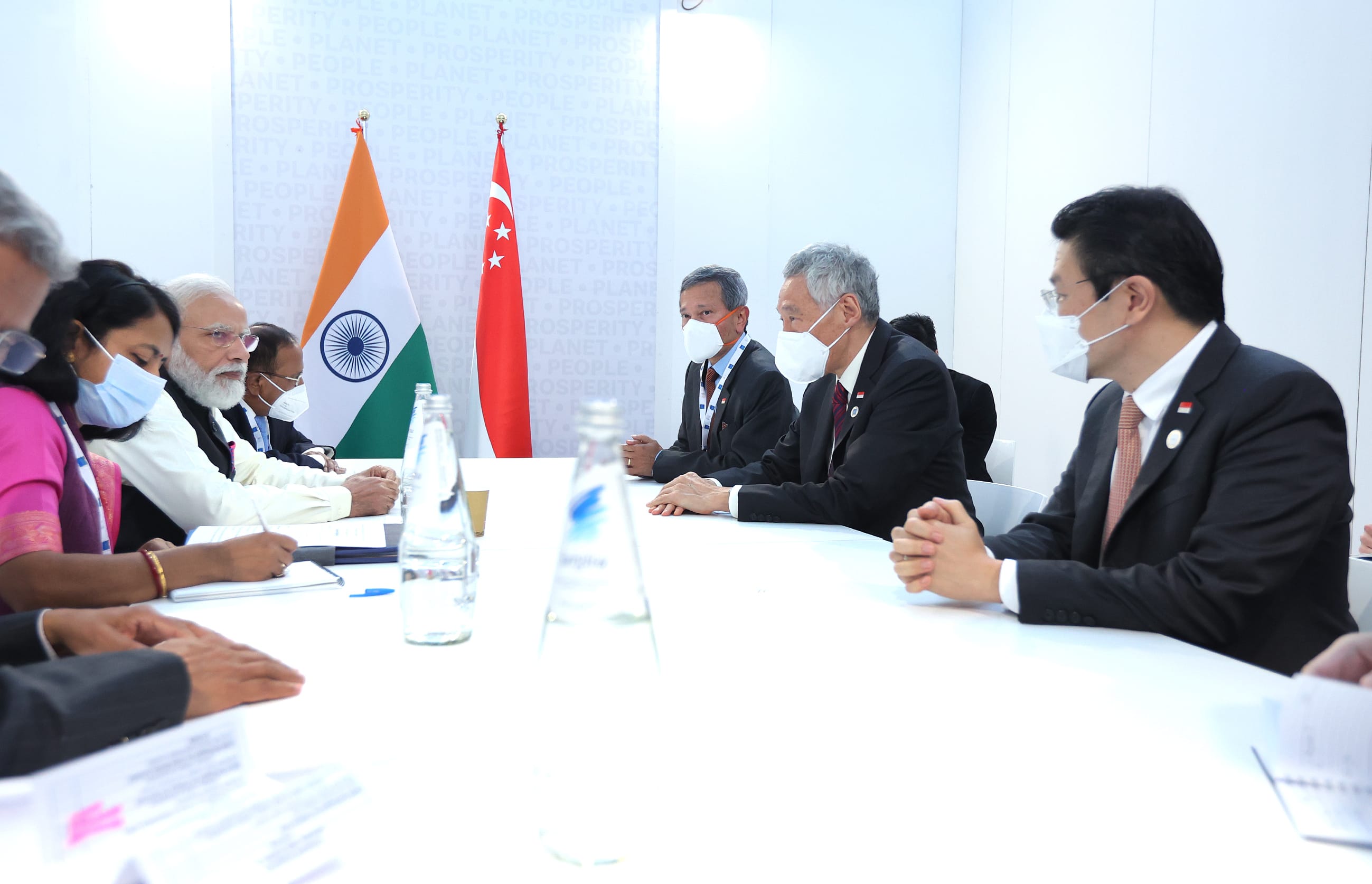 People in suits at a table with the flags of India and Singapore behind them.