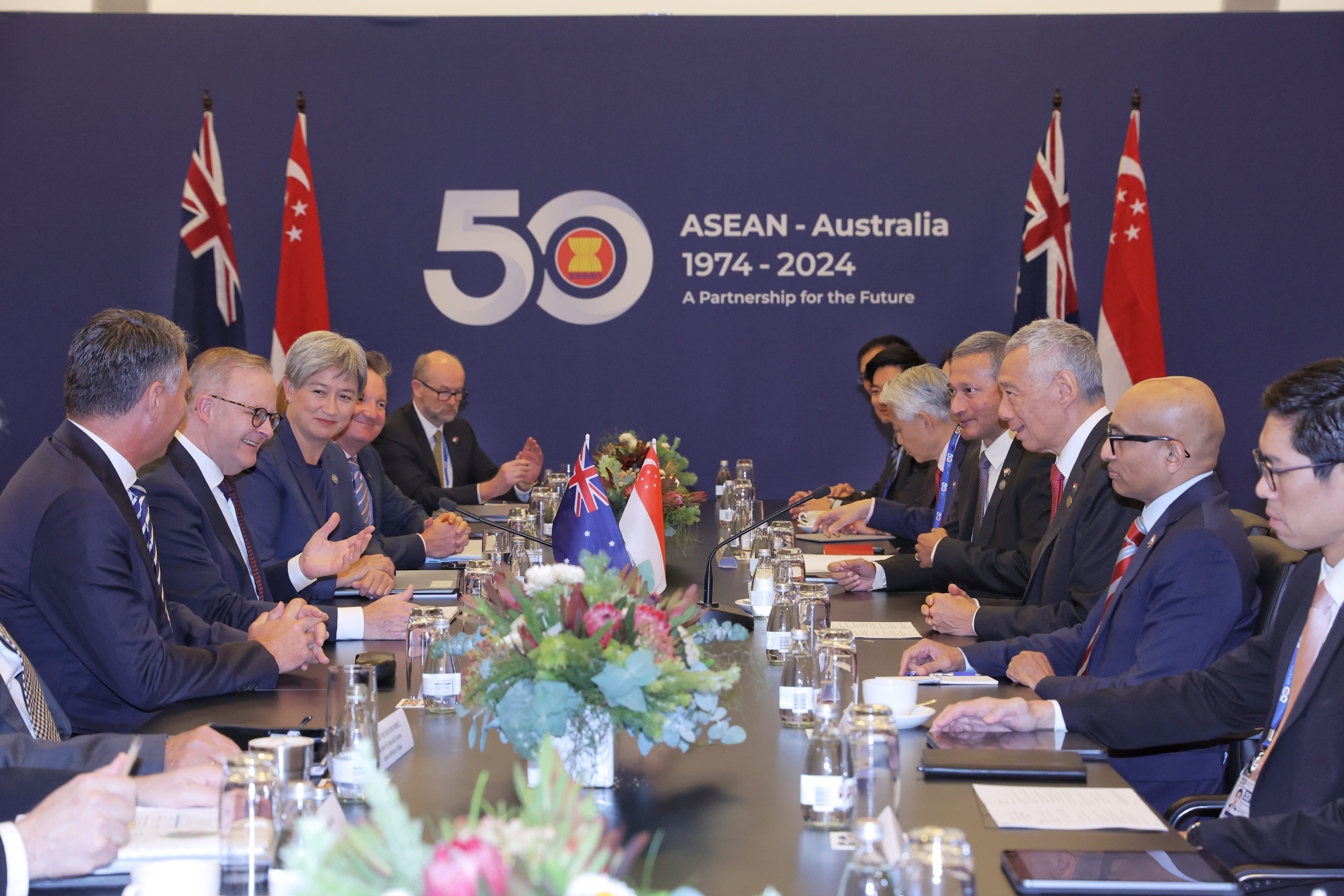 People at a long table in suits under ASEAN-Australia 1974-2024 banner. Flags of Australia, Singapore visible.
