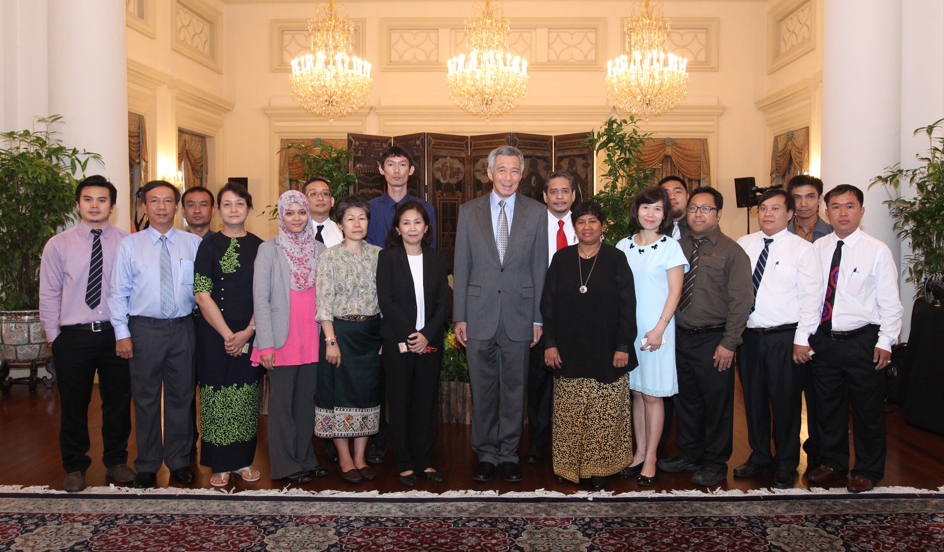 Group portrait with Lee Hsien Loong in a grey suit, standing in an ornate hall under chandeliers.