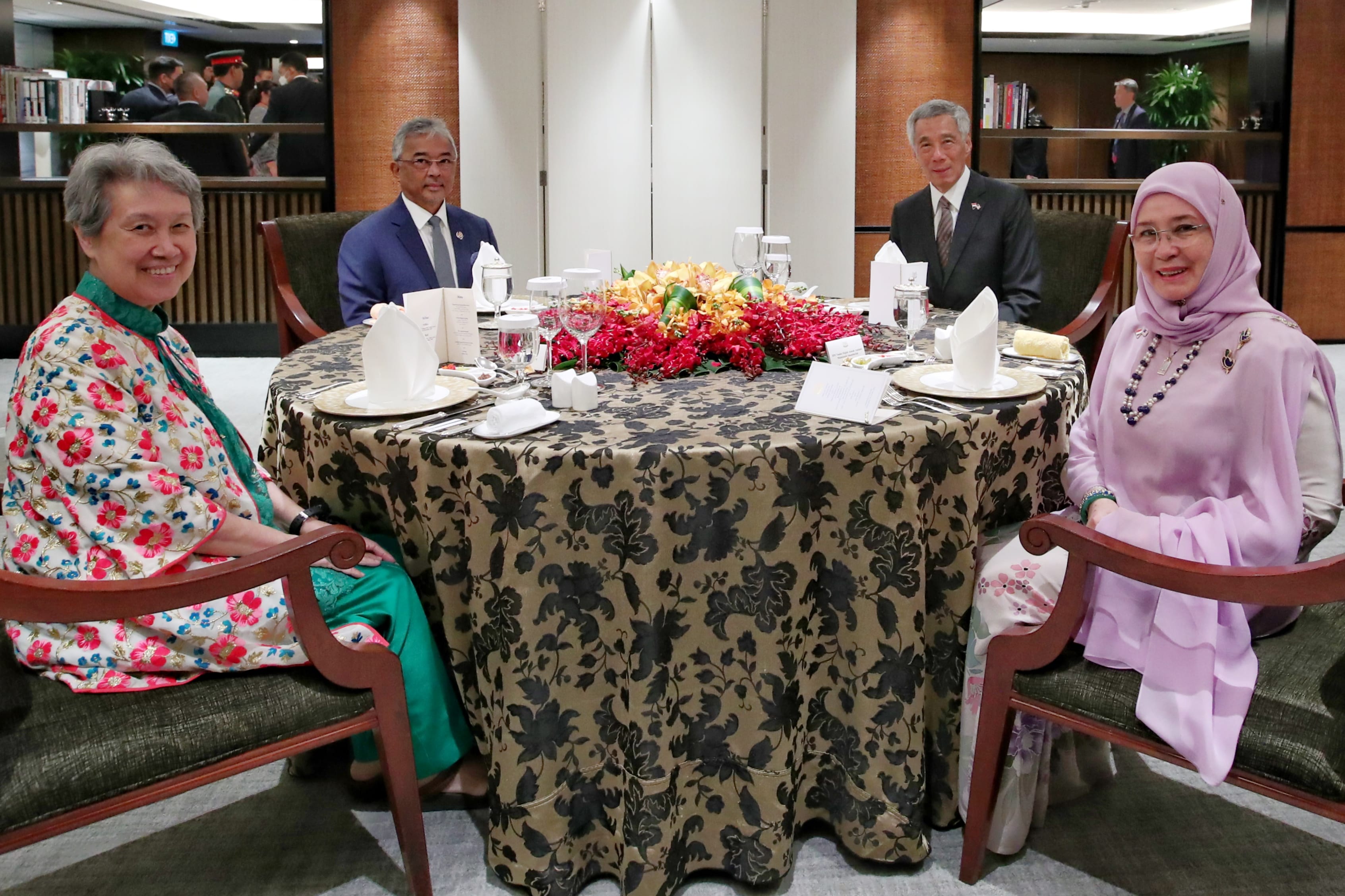 Four people at a round table with place settings and a floral centerpiece.