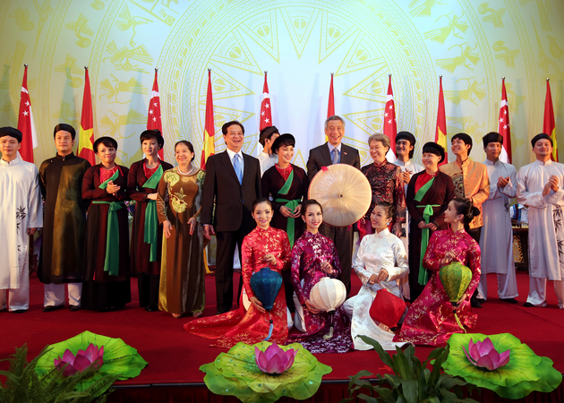 Group of people with flags of Vietnam and Singapore in background. Women wear Áo dài.