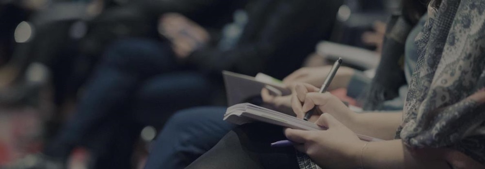 Close-up of people seated and writing notes during a conference or forum session.