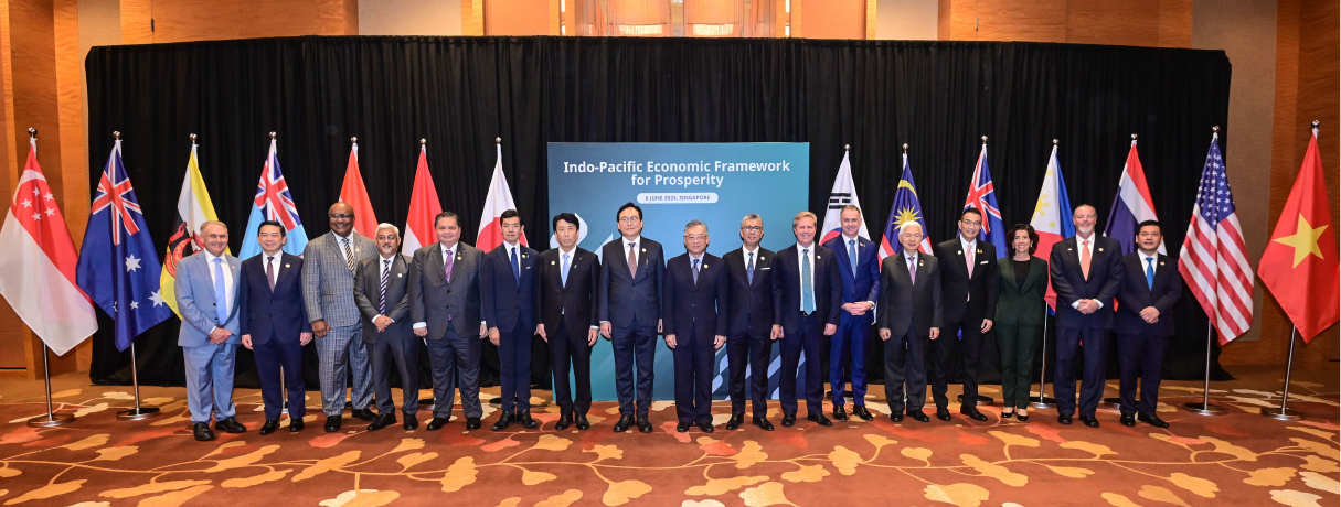 Ministers poses for a photo with flags behind them.