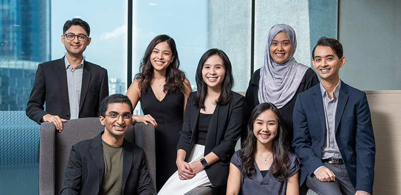 Seven MTI professionals posing together in business attire in an office setting.