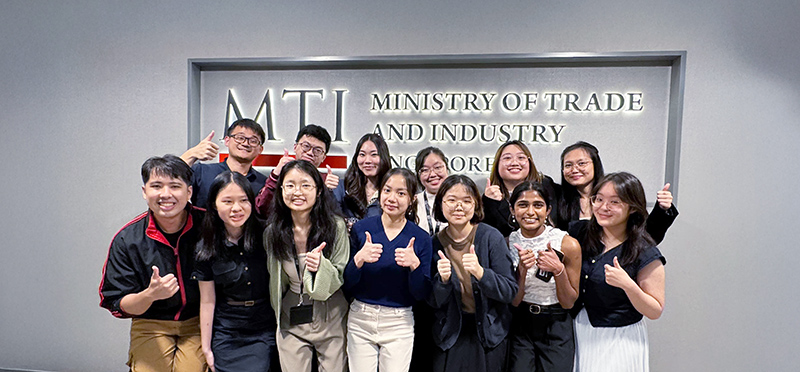 MTI interns posing together with thumbs up in front of MTI signboard.