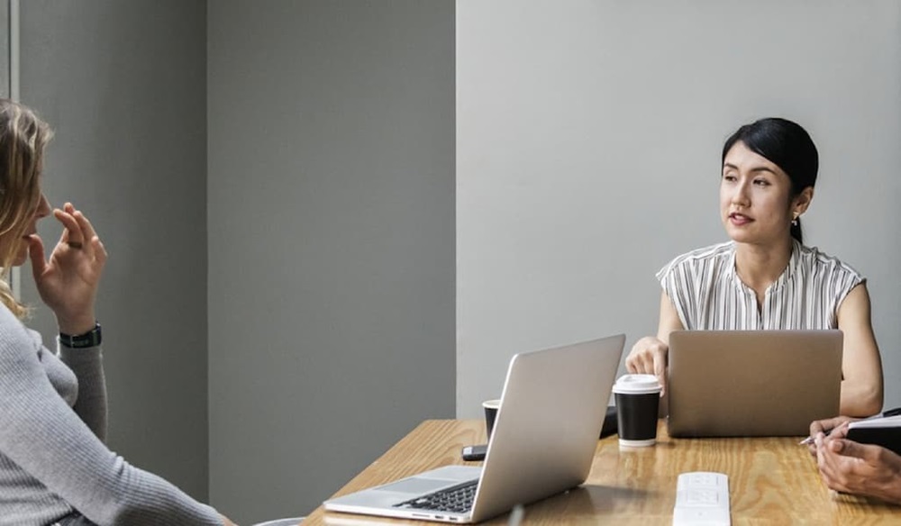 Three people in a discussion around a table with laptops and coffee cups.