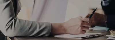 Close-up of person holding a pen over a clipboard during a discussion or meeting.
