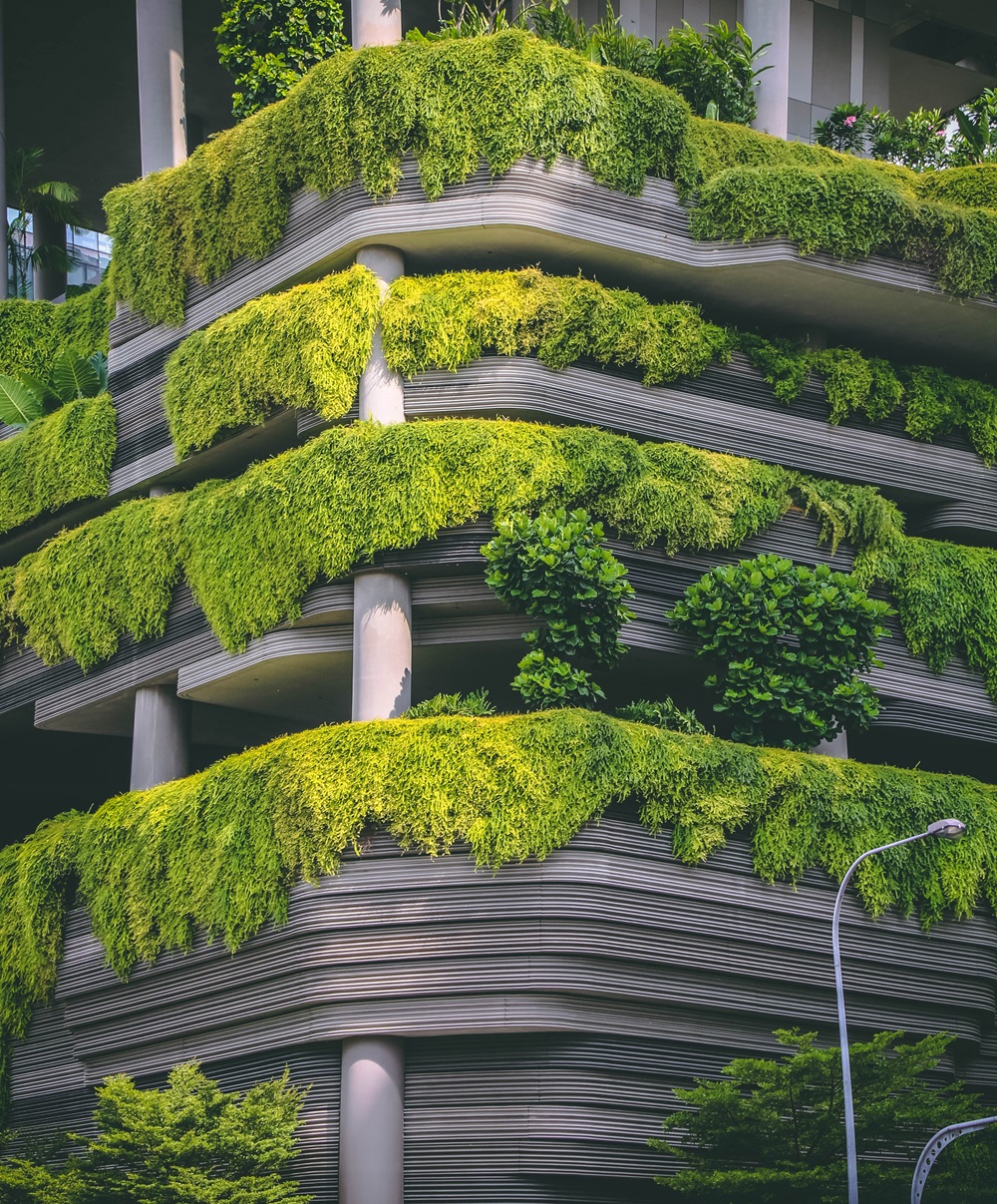 A building facade with layered, curved balconies draped in lush green foliage, forming a vertical garden effect.