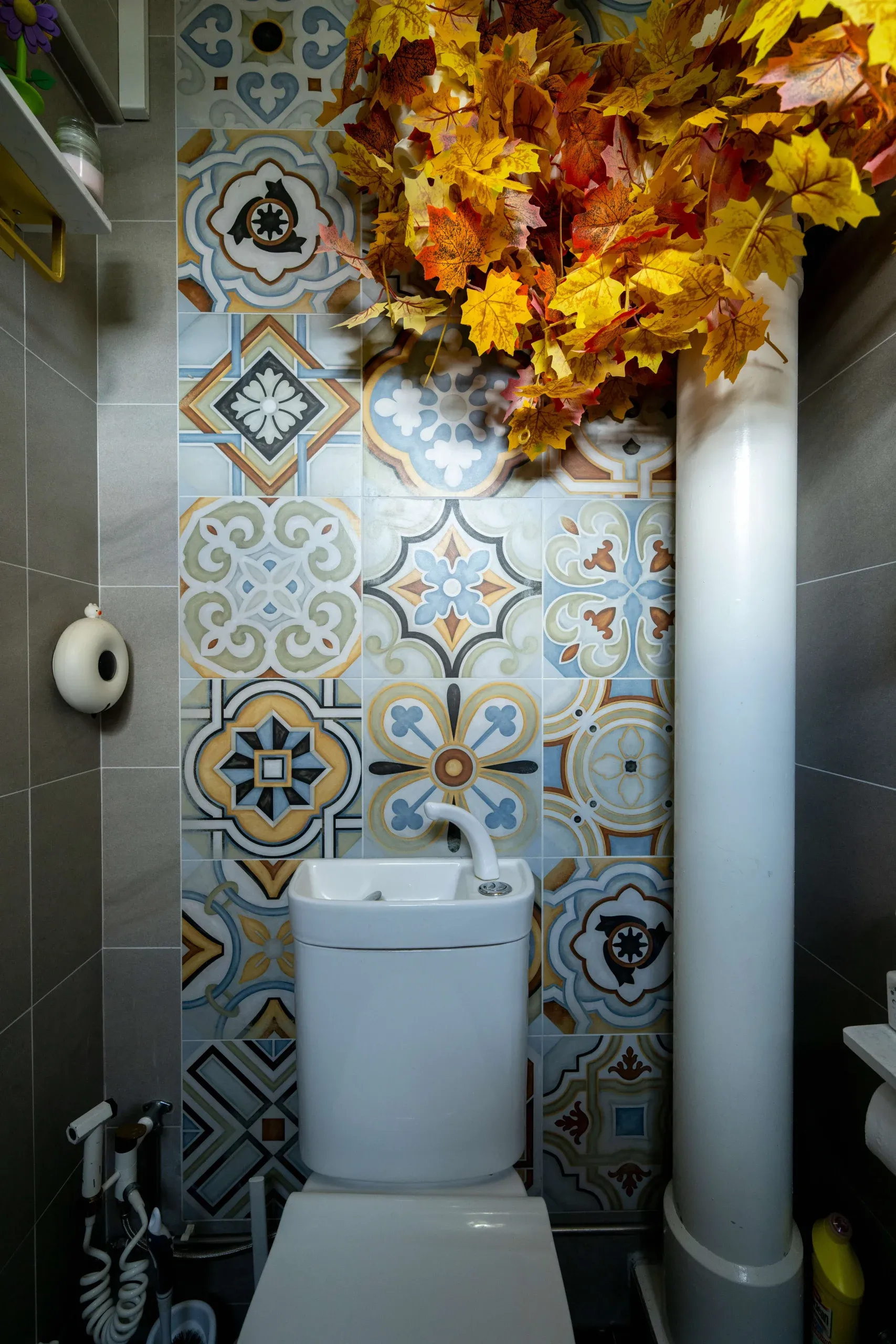 A toilet with autumn foliage hung above, and decorative wall tiles.