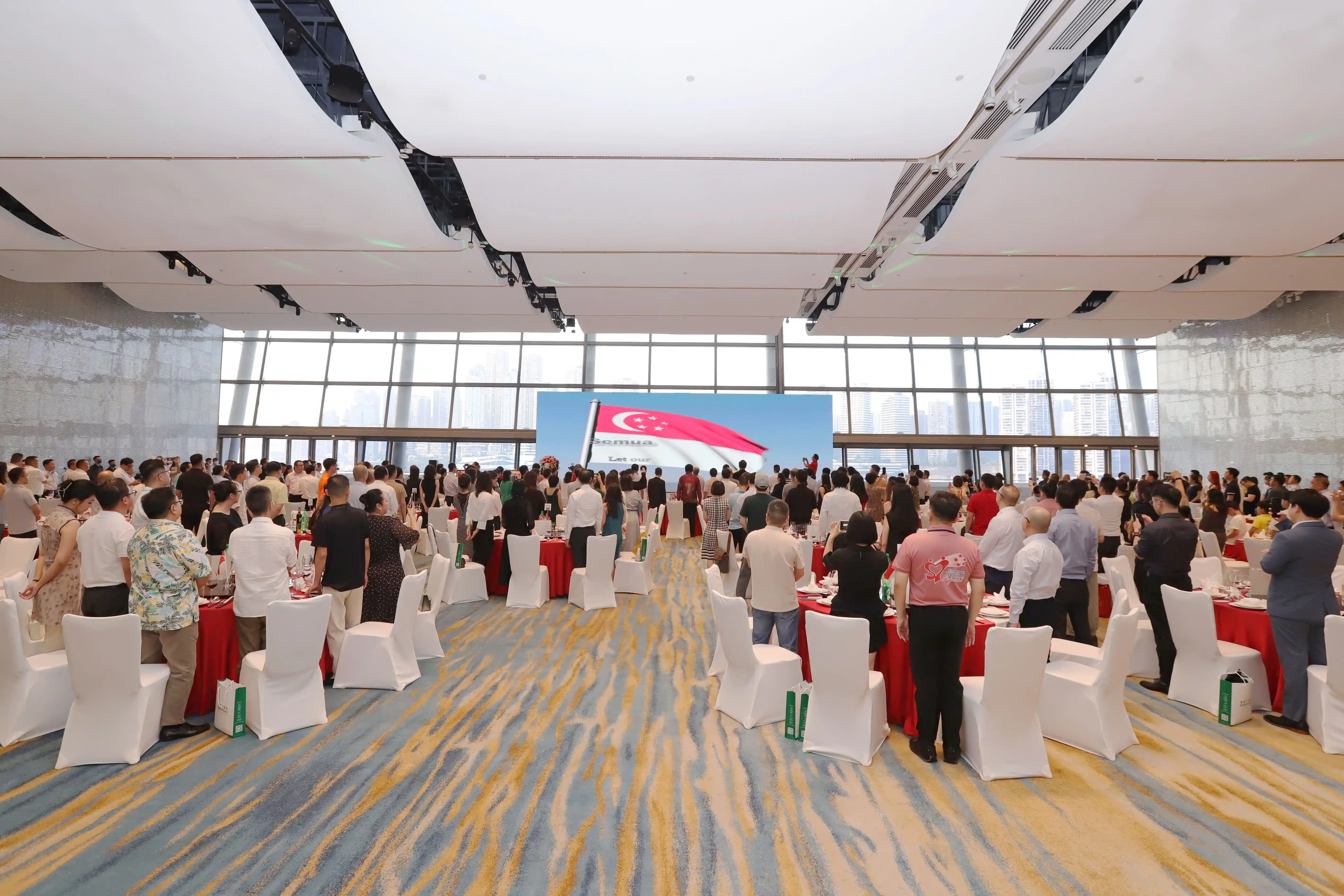 Large room with people, tables, chairs, and a screen showing the Singapore flag.