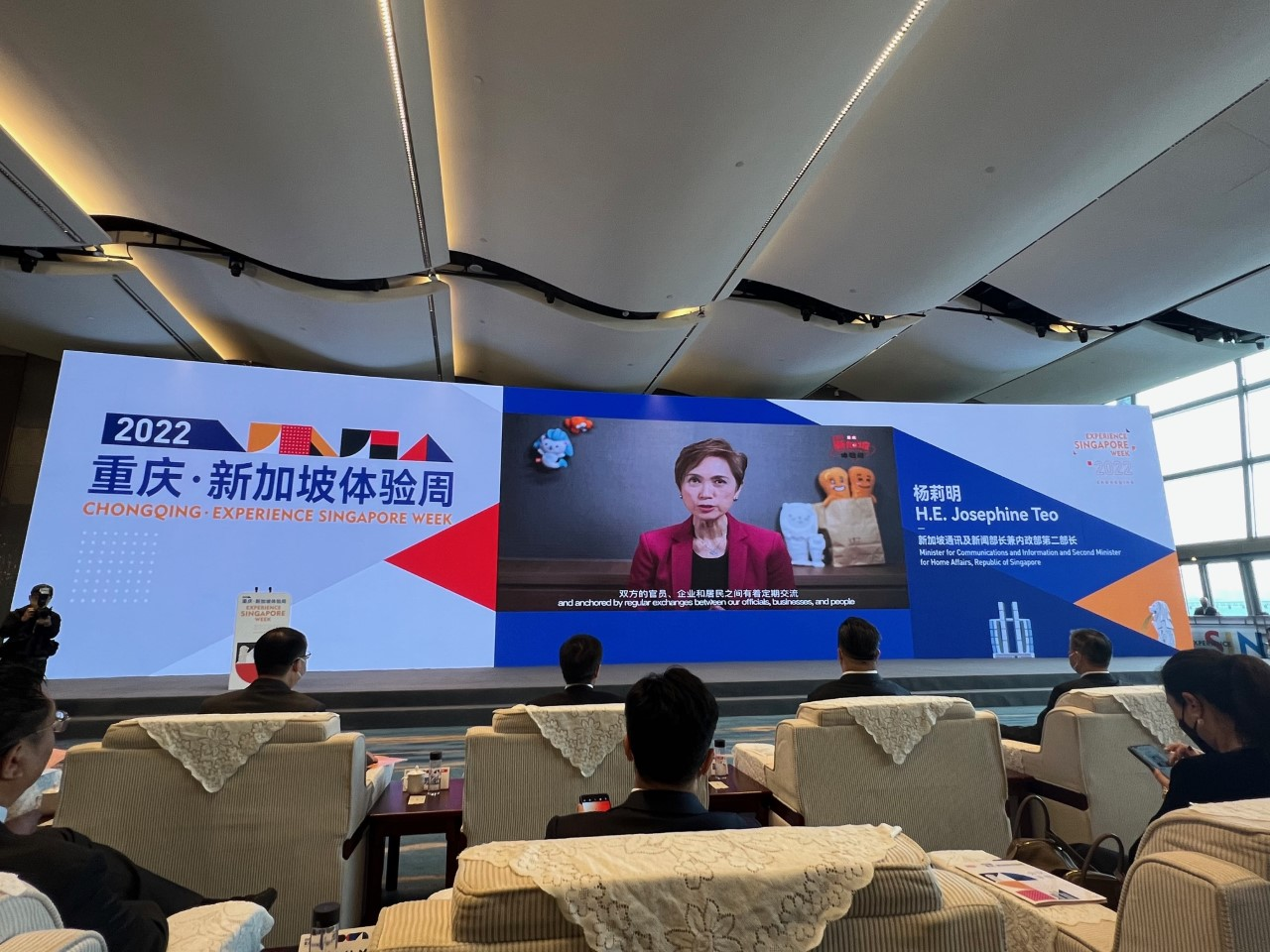 "Chongqing - Experience Singapore Week" event, Josephine Teo on screen with attendees in foreground.