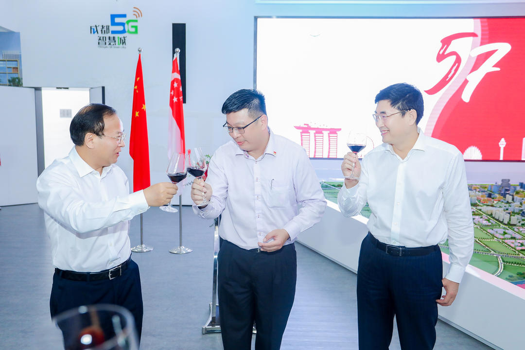 Three men in dress shirts toasting red wine. Flags of China and Singapore stand in the background.