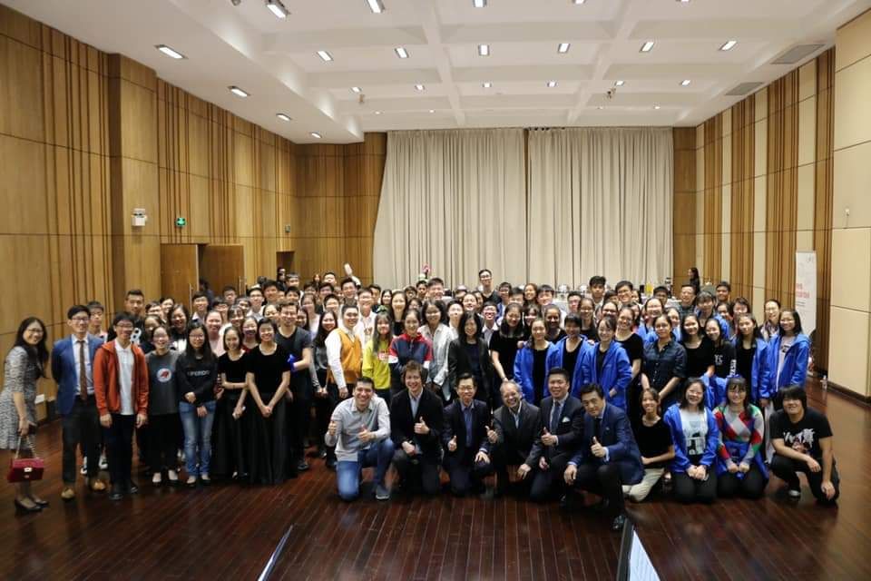 Large group of people in a wood-paneled hall, some giving thumbs up.