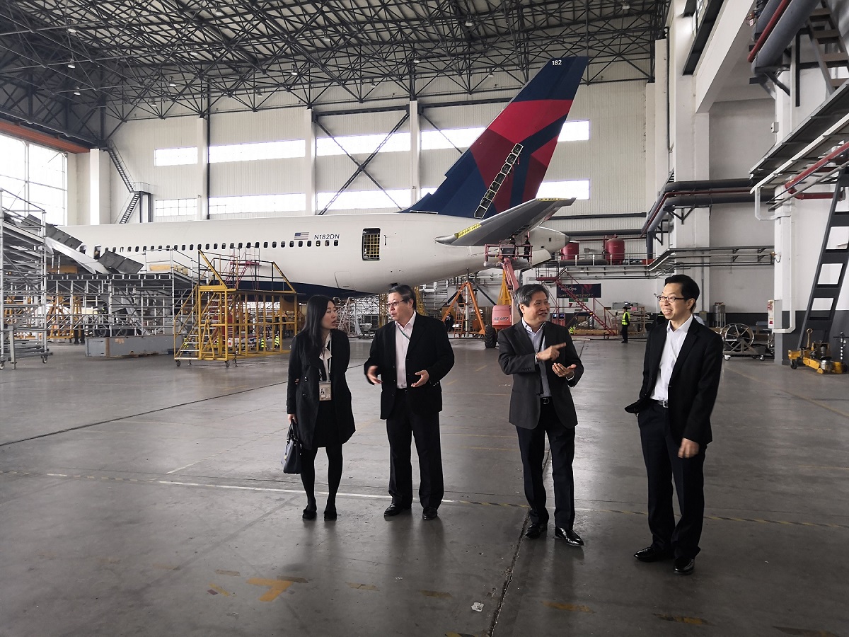 Four people in suits stand in an aircraft hangar with a Delta Airlines plane.