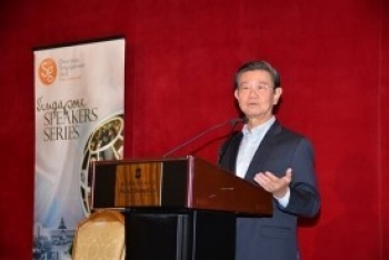 Man at podium with "Singapore Speakers Series" banner against a red wall.