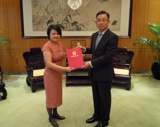 Two people exchange a red folder in an office setting.