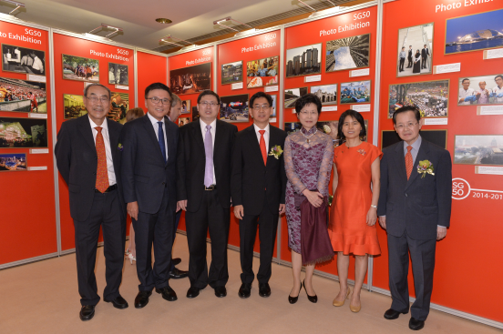 Group of seven people stand at a "SG50 Photo Exhibition" with photos on red panels.