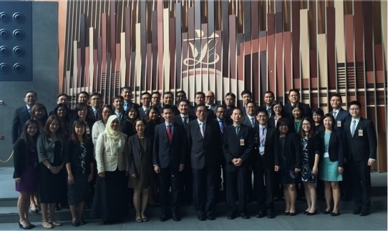 Large group of people in business attire, posing in front of a wall with vertical bars and a logo.