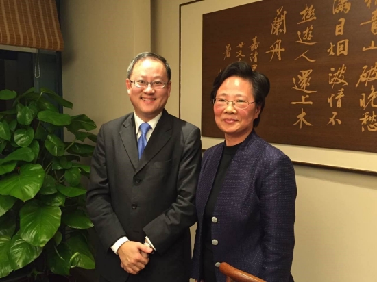 Two people pose in formal attire before a wall hanging with calligraphy.