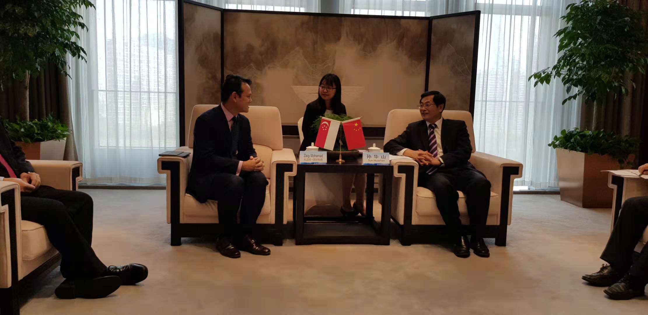 Business meeting with flags of Singapore and China on table. People are in suits.