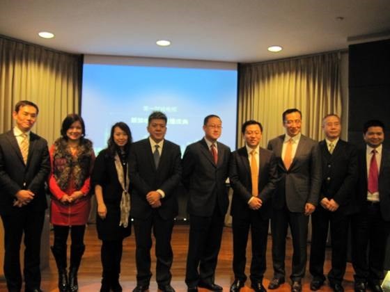 Group of eight people in business attire standing on a wooden floor in front of a screen.
