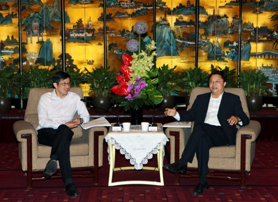 Two men in suits seated facing each other; table with flowers and microphones between them.
