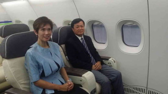 Two people sit in first-class airplane seats next to two windows.