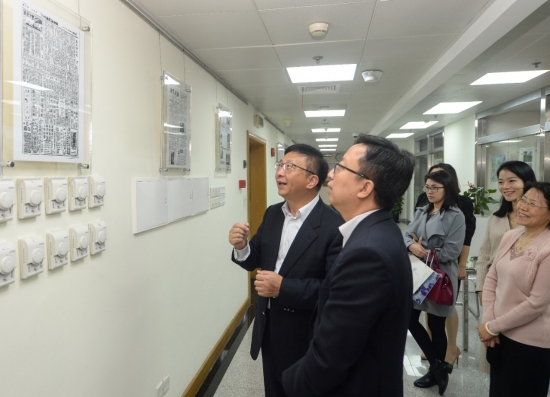 People viewing framed articles and white thermostats on a hallway wall.