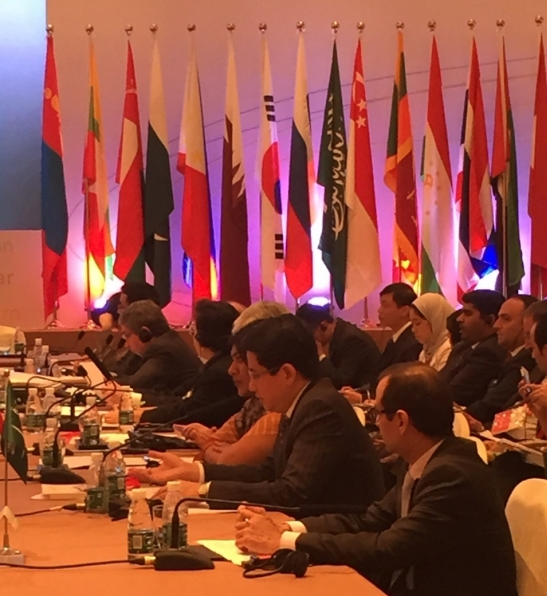 People at a conference table, country flags are displayed behind them.
