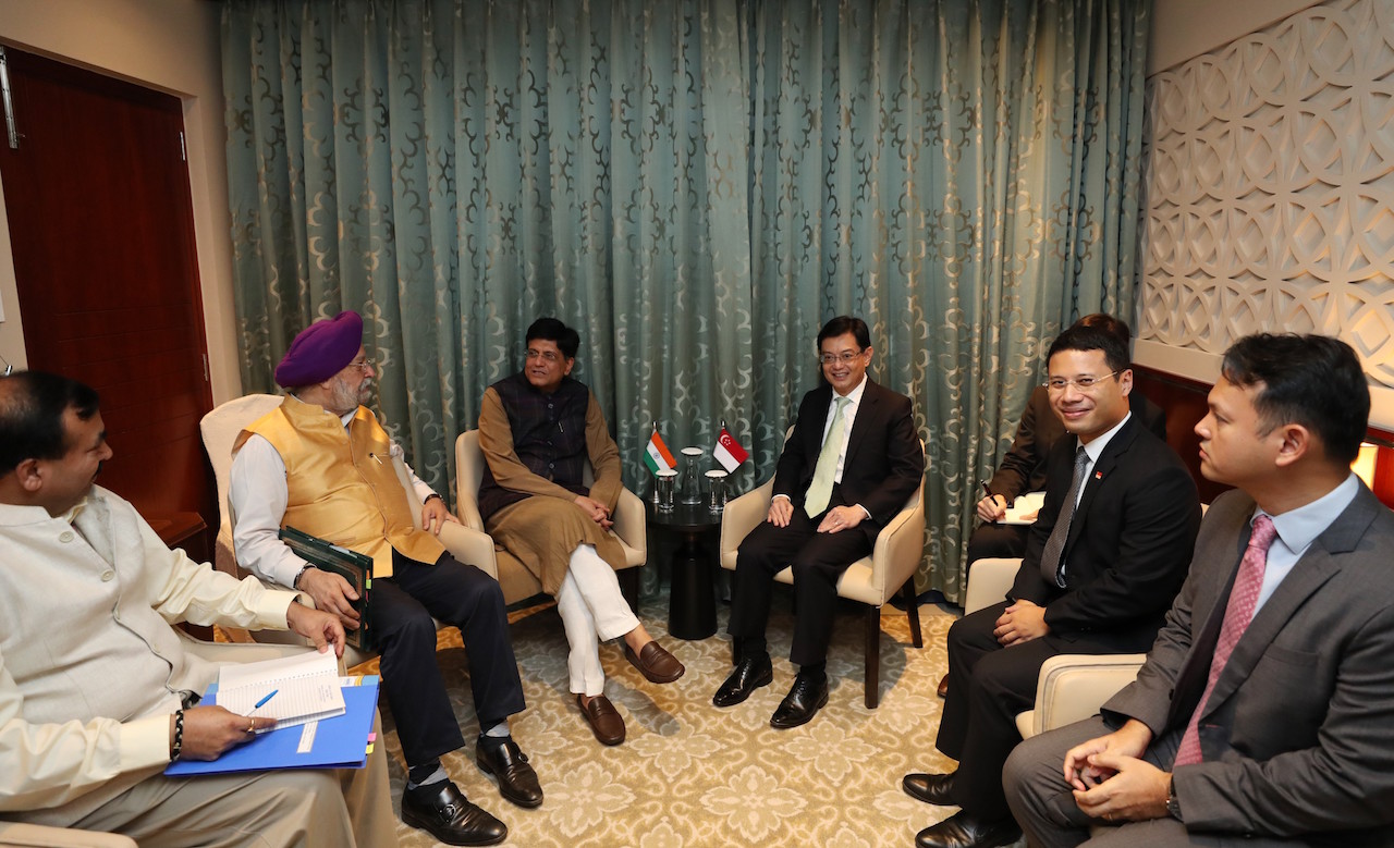 Group of men in suits and formal wear meet in a room. Indian and Singapore flags in the center.