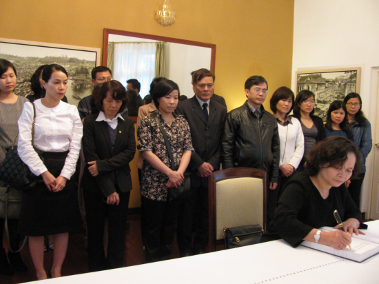 Group of people watching a woman in black sign a book on a white table.