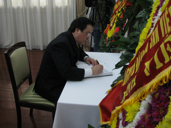 Man in suit signing guestbook next to floral wreath.