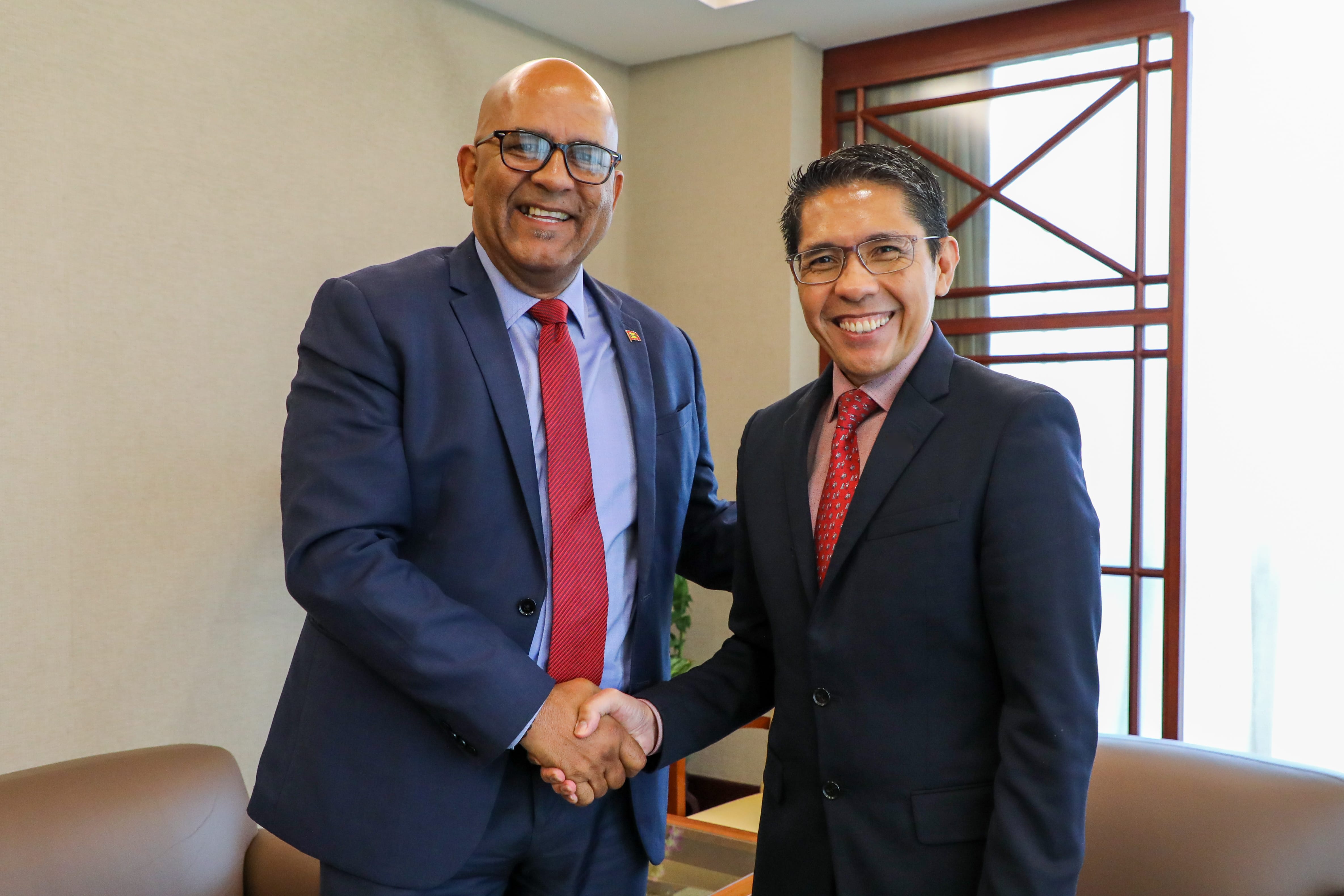 Two men in suits and ties are shaking hands in an office setting.