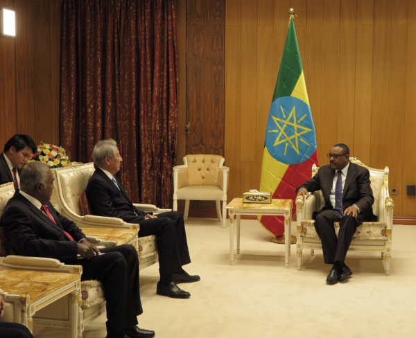 Three men in suits sit facing Abiy Ahmed next to an Ethiopian flag.