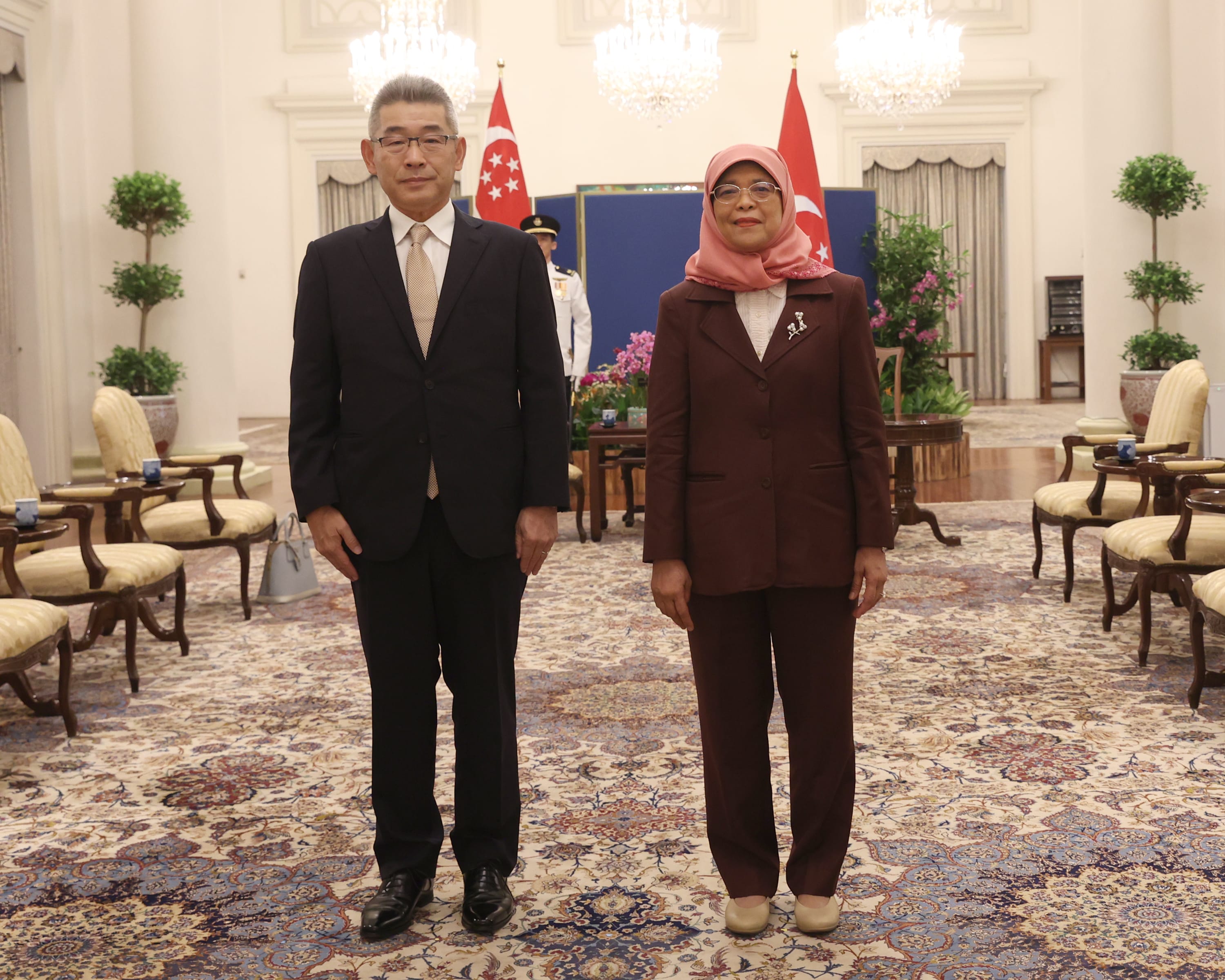 Man and Halimah Yacob stand in front of Singapore flags in a formal room.