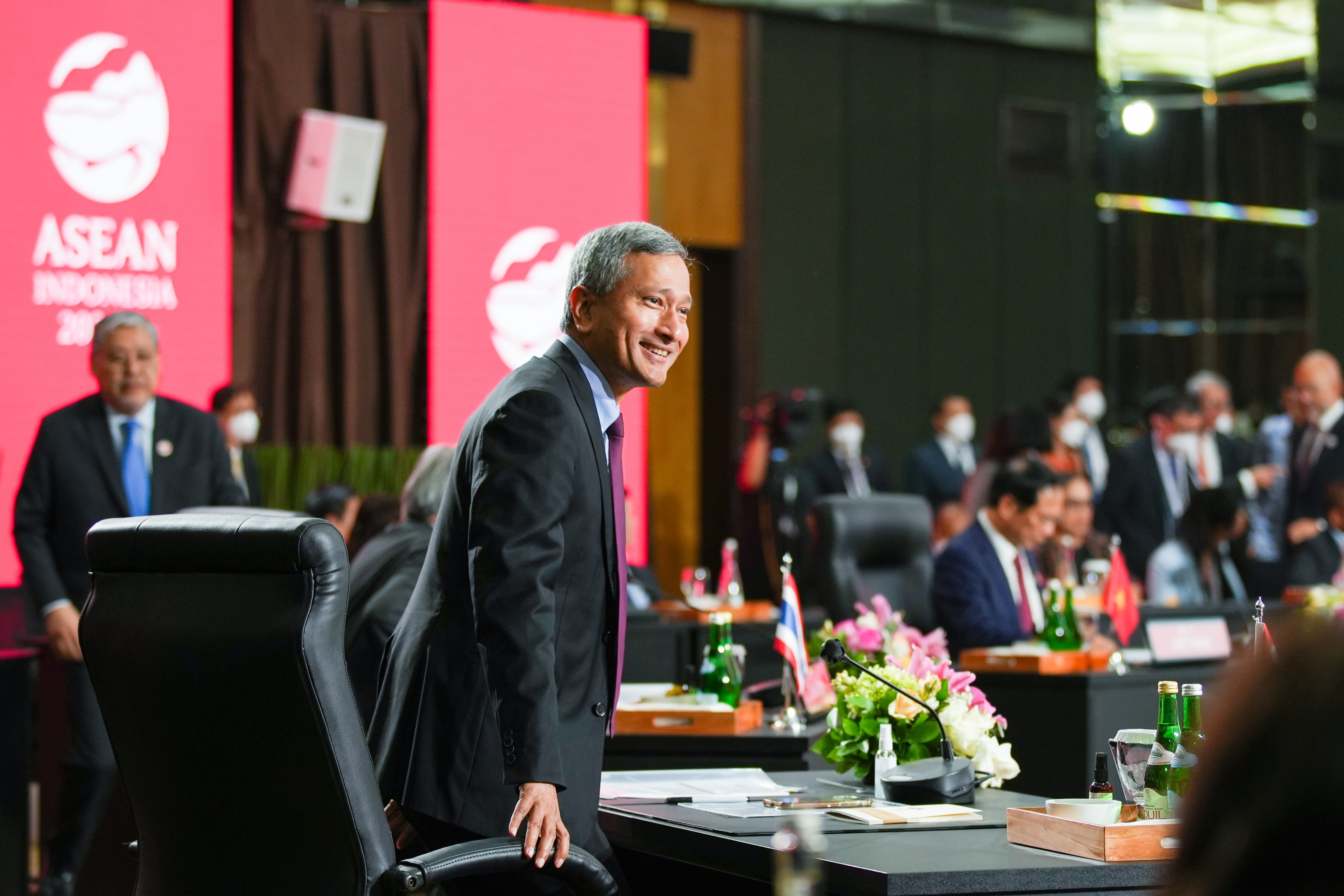 Smiling man in suit stands at a meeting table with ASEAN Indonesia 2023 logo in background.